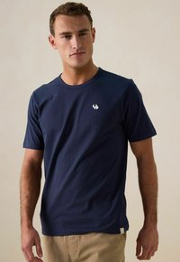 Navyblauwe katoenen t-shirt met een ronde halslijn, korte mouwen en een klein wit logo op de linkerborst. Soepele textuur, casual pasvorm.