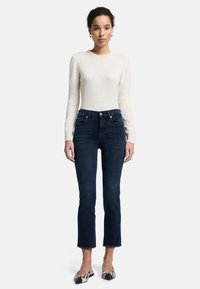 Pull long à manches longues en crème clair ajusté ; jean droit bleu foncé avec ourlet brut ; ballerines à motif avec embout noir et impression de serpent.