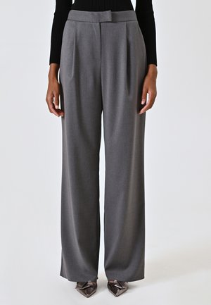 Pantalons gris à large jambe avec des plis, taille mi-haute, coupe ajustée et texture lisse. Associés à des chaussures à talons avec un bout pointu.