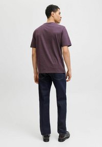 Short-sleeve, crew-neck t-shirt in dark purple, made from cotton blend fabric. Worn with straight-leg dark blue jeans and black shoes.