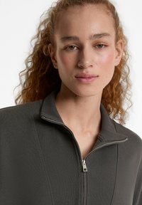 Dunkelgraue, gerippte Zip-Jacke mit Stehkragen, ausgestattet mit einem silbernen Reißverschluss und glatter Stoffstruktur.