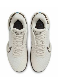 Weiße Sportschuhe mit einem strukturierten Mesh-Obermaterial, braunem Nike-Swoosh, Schnürdesign und hellblauen Akzenten. Geeignet für Sport.