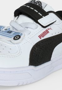 Λευκό και μαύρο sneaker Puma με άσπρα κορδόνια, μαύρο λουράκι και μια μπλε διακόσμηση σε σχήμα αυτοκινήτου στην περιοχή των δαχτύλων.