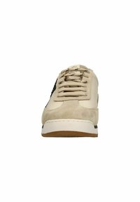 Beige sneaker van suede en leer, met platte veters, een witte tussenzool en een bruine rubberen zool. Bevat een zwarte accent aan de zijkant.