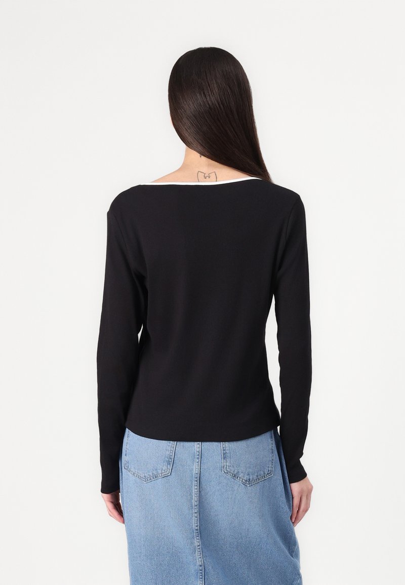 Top nero a maniche lunghe con scollo ampio e bordo bianco, abbinato a una gonna in denim azzurro chiaro con tasche posteriori e design dritto.