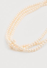 Τρεις σειρές μικρών, στρογγυλών λευκών μαργαριταριών με λείο, γυαλιστερό περίβλημα, τοποθετημένες κοντά η μία στην άλλη σε φωτεινό φόντο.