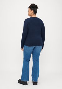 Meriharmaa teksturoitu neule pyöreällä kauluksella ja pitkillä hihoilla, yhdistettynä vaalean sinisiin leveälahkeisiin farkkuihin ja paksuihin mustiin kenkiin.