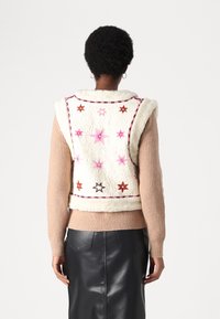 Faux fur vest in cream with pink and brown star embroidery, thick collar, and pink trim; paired with a beige ribbed sweater and black leather skirt.