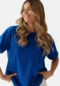 Niebieska bawełniana koszulka z okrągłym dekoltem, krótkimi rękawami i luźnym krojem. Gładka tekstura i podwinięte mankiety.