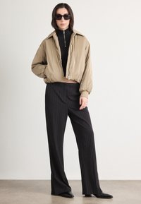 Cropped beige jacket with elastic hem, paired with black formal striped pants. Model wears a black turtleneck and oversized black sunglasses.