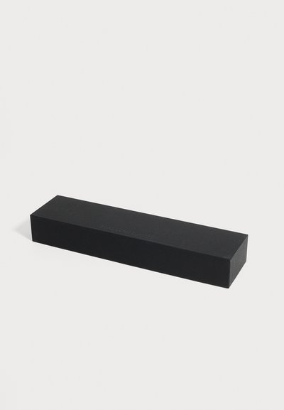 Longue boîte rectangulaire noire avec un texte discret "EATON LABS" en haut, affichée sur un fond gris clair uni.