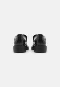 Scarpe in pelle nera dal design elegante, con punte arrotondate e tacchi neri spessi. Presentano un marchio discreto sul tallone e una texture liscia.
