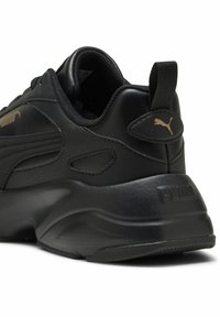 Schwarzer Sport-Schuh aus glattem Lederobermaterial, gepolstertem Kragen, Gummisohle und goldenem Puma-Logo an der Seite sowie an der Ferse.