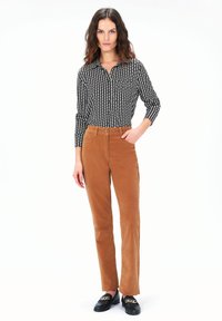 Camisa de botones negra y blanca con estampado, de manga larga, combinada con pantalones de pata de gallo color tierra y mocasines negros con detalles dorados.