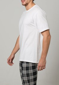 Camiseta blanca de algodón con cuello redondo, mangas cortas y un ajuste relajado, combinada con pantalones de pijama a rayas grises con acentos azules.