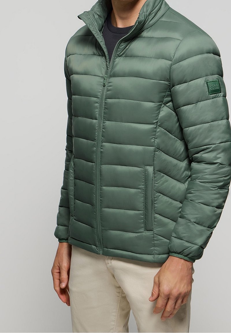 Zelená prošívaná péřová bunda se zapínáním na zip vpředu, vysokým límcem, dvěma bočními kapsami a nášivkou s logem na levém rukávu. Hladká textura.