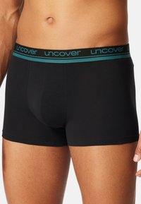 Black boxer briefs featuring a contrasting teal waistband with "uncover" branding, made of smooth stretch material for comfort.