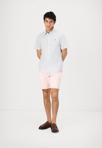 Lys blå kortermet skjorte med knapper og subtil tekstur, kombinert med rosa shorts og brune loafere. Har en liten logo på brystet.