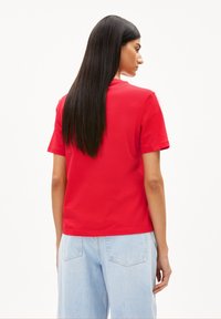 Rode katoenen t-shirt met korte mouwen en rechte snit, bekeken vanaf de achterkant. Gekoppeld met lichtblauwe denim broek.