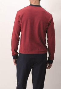 Felpa rossa con scollatura rotonda, dettagli in blu navy sul colletto e sui polsini, e un tessuto testurizzato. Presenta maniche lunghe e un design aderente.