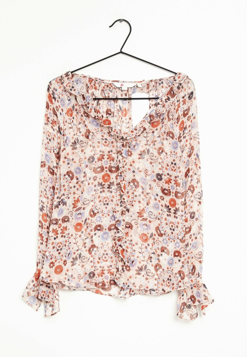 Blouse à manches longues avec col et poignets à volants, ornée d'un motif floral aux teintes de rouge, orange, violet et beige, suspendue sur un cintre noir.