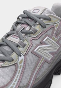 Κοντινό πλάνο ενός αθλητικού παπουτσιού New Balance σε γκρι και παστέλ ροζ αποχρώσεις, με υφή δροσερού διχτυωτού υφάσματος και παχιά γκρι κορδόνια δεμένα προσεκτικά.