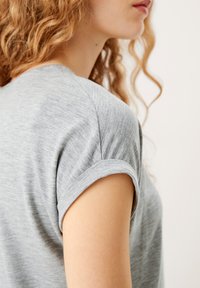 Szary T-shirt z krótkim rękawem o gładkiej fakturze, z podwiniętymi mankietami i luźnym krojem, wyeksponowany z boku.