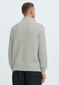 Hellegrauer, gerippter Strickpullover mit hohem Kragen und überschnittenen Schultern, der eine lockere Passform und eine weiche Textur aufweist.