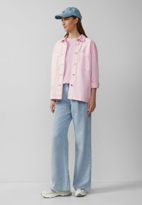 Jasnoróżowa kurtka dżinsowa na różowej bluzce, w połączeniu z jasnoniebieskimi spodniami dżinsowymi o szerokich nogawkach i jasnoniebieską czapką, zdobiona minimalnymi elementami metalowymi.