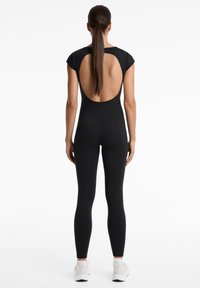 Zwarte bodysuit met korte mouwen en een grote open rug. Glad materiaal met een aansluitend ontwerp, gecombineerd met witte sportschoenen.
