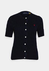 Marinblå kortärmad cardigan i kabelstickat tyg med rund halsringning, sex vita knappar och en liten röd logga på bröstet.