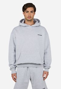 Sudadera de algodón gris con un bolsillo frontal, puños y cintura acanalados, que presenta el texto negro "PEGADOR" en el pecho. Pantalones de chándal grises a juego.