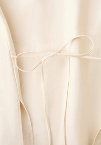 Tissu crème avec une fine ceinture nouée en un simple nœud à la taille d'un vêtement.