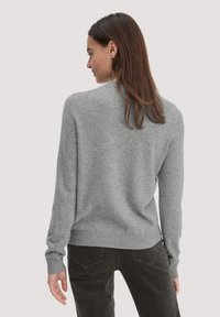 Grauer Strickpullover mit langen Ärmeln, geripptem Saum und Rundhalsausschnitt. Weiche Textur und lockere Passform, kombiniert mit dunklen kordeligen Hosen.