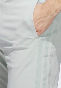 Light grey athletic pants with a smooth texture, featuring side pockets and three vertical stripes down the outer leg.