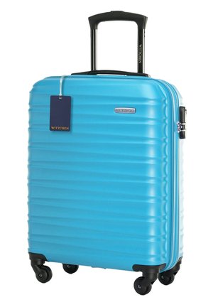 Jasnoniebieska walizka z twardą skorupą, wyposażona w cztery czarne kółka, teleskopową czarną rączkę oraz ciemnoniebieską zawieszkę bagażową.