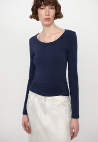 Marineblaue Langarmbluse mit einem runden Ausschnitt, aus einem glatten Stoff, figurbetontem Design, kombiniert mit einem silbernen strukturierten Rock.