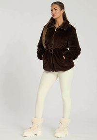 Bruine nepbont jasje met rits, gathered taille en zijzakken. Gepaarde met crèmekleurige leggings en beige laarzen met bontvoering.