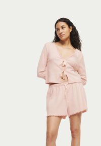 Lichtroze loungewear set met een cropped top met striksluitingen en geribbelde textuur, gecombineerd met shorts met elastische taille en scalloped randen.