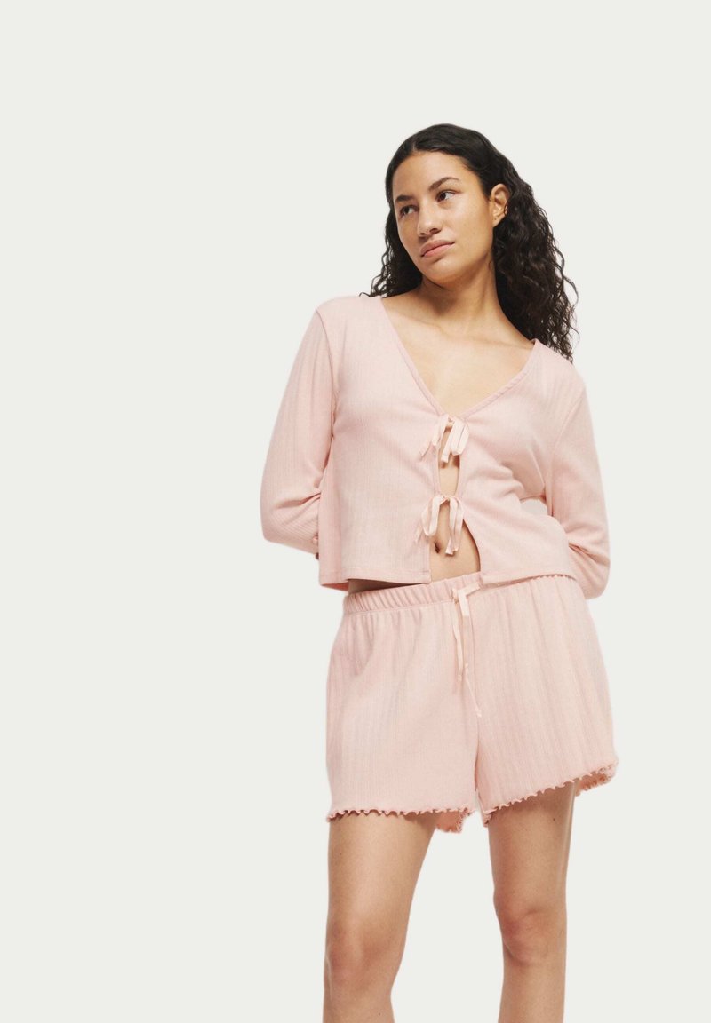 Lichtroze loungewear set met een cropped top met striksluitingen en geribbelde textuur, gecombineerd met shorts met elastische taille en scalloped randen.