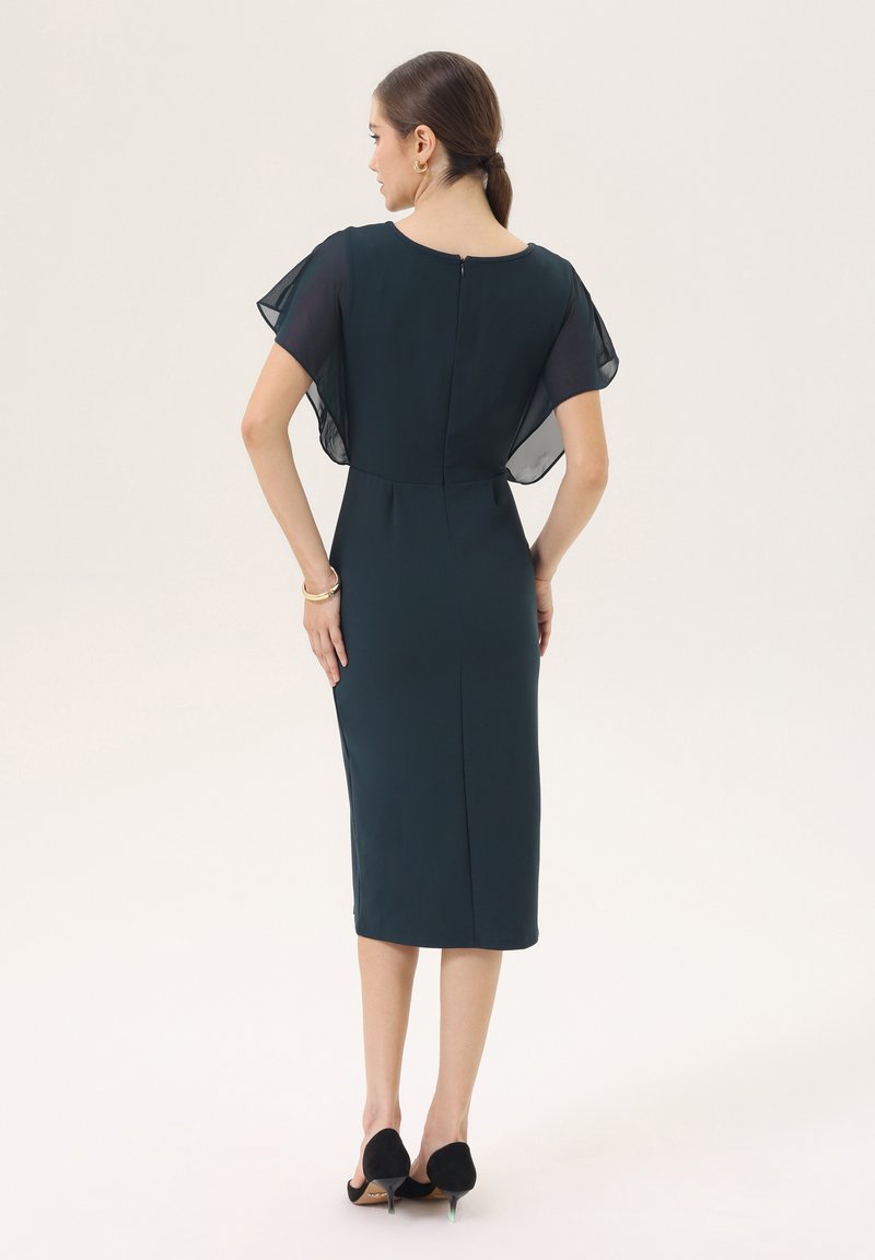 Donkergroen jurk tot knielengte met korte, doorschijnende vlindermouwen, rits aan de achterkant en een getailleerd silhouet. Textuurstof met een gladde afwerking.