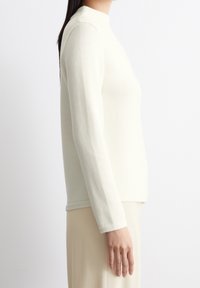 Maglione bianco a maniche lunghe con colletto alto, taglio dritto e tessuto testurizzato. Dettagli delle cuciture su spalle e orlo.
