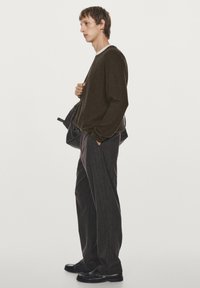 Mørkegrøn striktrøje med lange ærmer, parret med mørke stribede bukser. Modellen holder en sort taske og har sorte loafers på.