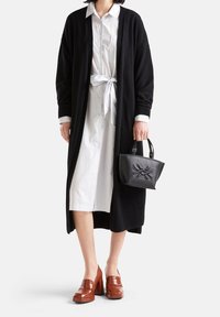 Černý dlouhý kardigan přes bílé pruhované košilové šaty s vázaným pasem, doplněné hn�ědými masivními mokasínami a malou černou kabelkou.