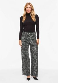 Haut à col roulé noir côtelé associé à un pantalon gris taille haute à jambes larges avec un motif léopard noir. Talons pointus noirs.