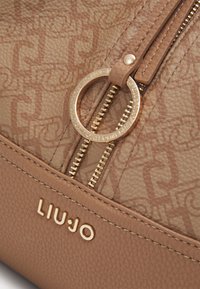 Brun lædertaske med et tekstureret mønster, guldfarvet hardware, lynlås lukning og brandnavnet "LIU-JO" præget foran.