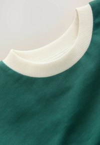 Grüner Kapuzenpullover mit einem gerippten, cremefarbenen Rundhalsausschnitt und weichem Material, aus einem Winkel gezeigt, der das Kragen-Design hervorhebt.