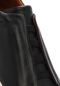 Czarny skórzany botek z elastycznymi panelami po bokach i brązową wewnętrzną wyściółką widziany z bliska.