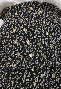 Abito nero a fiori con motivi di foglie bianche e dorate, vita elastica, design a balze a strati e tessuto leggero.
