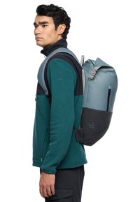 Zaino grigio e nero con design a roll-top, realizzato in tessuto resistente. Presenta spallacci regolabili, cerniera laterale e dettaglio testuale stampato.